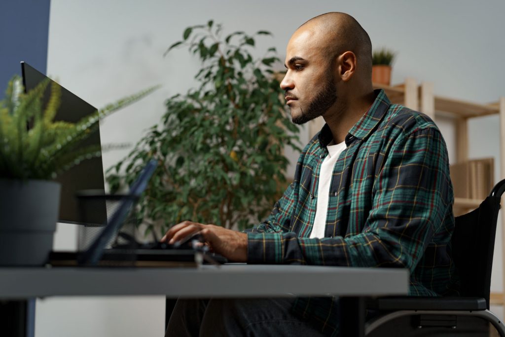 telework accommodations, man sitting in a wheel chair working from home using a computer.
